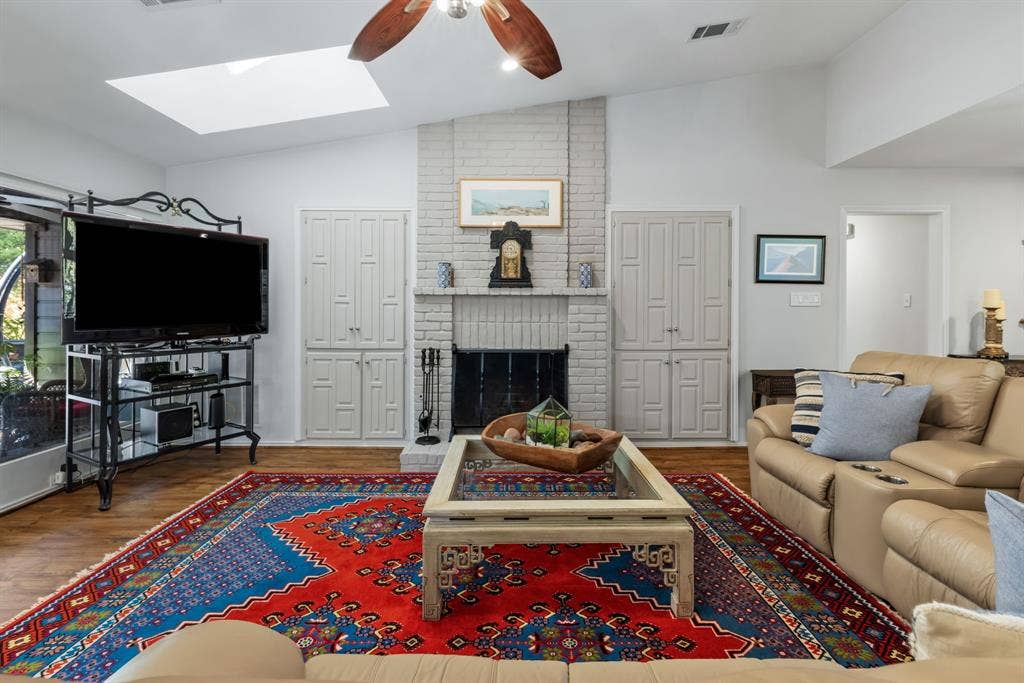 6803 Fernshaw Drive, Dallas, TX 75248 Vaulted ceiling with skylight, brick fireplace, wood-finish flooring, ceiling fan, and built-in cabinetry