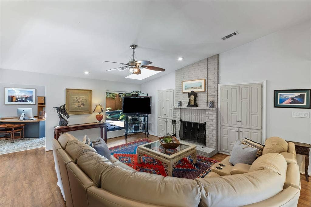 6803 Fernshaw Drive, Dallas, TX 75248 Vaulted ceiling, wood-finish flooring, brick fireplace with mantel, built-in cabinetry, and ceiling fan with integrated lighting