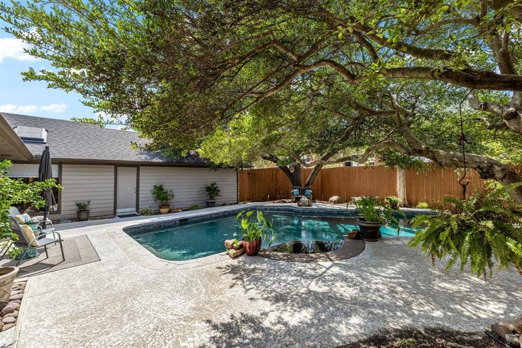 6803 Fernshaw Drive, Dallas, TX 75248 Private backyard featuring a swimming pool with a waterfall, mature trees, concrete patio, and a wood privacy fence