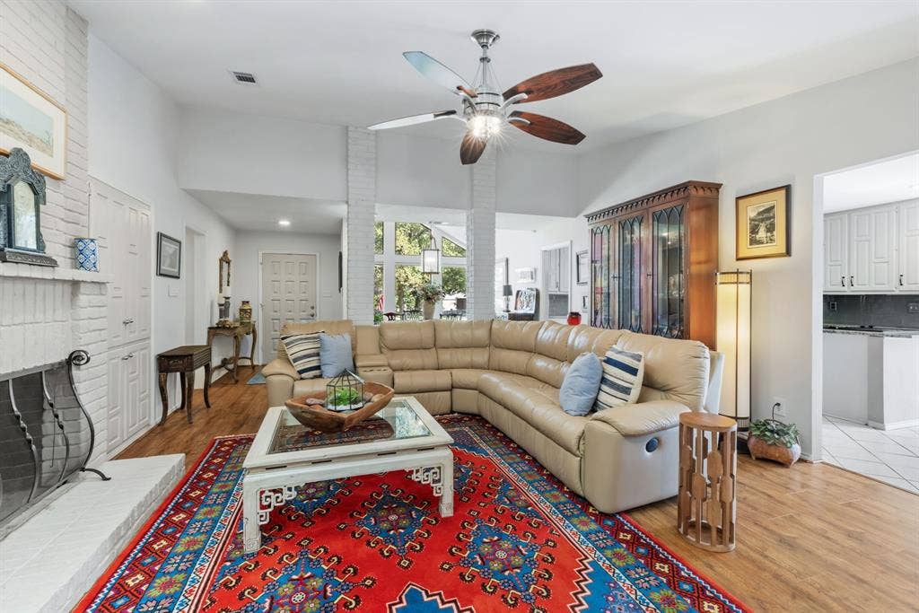 6803 Fernshaw Drive, Dallas, TX 75248 Vaulted ceilings, wood-finish flooring, white painted brick fireplace with hearth, and a contemporary ceiling fan