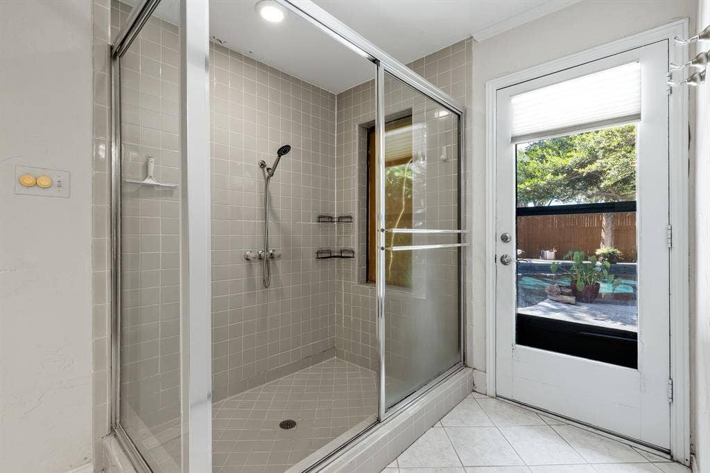 6803 Fernshaw Drive, Dallas, TX 75248 Tiled shower enclosure with a glass sliding door, built-in shelving, and an adjacent exterior door with a privacy blind