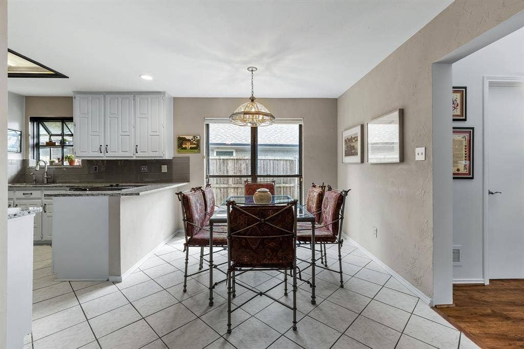6803 Fernshaw Drive, Dallas, TX 75248 White cabinetry, tile flooring, built-in breakfast bar, pendant lighting, and a large window