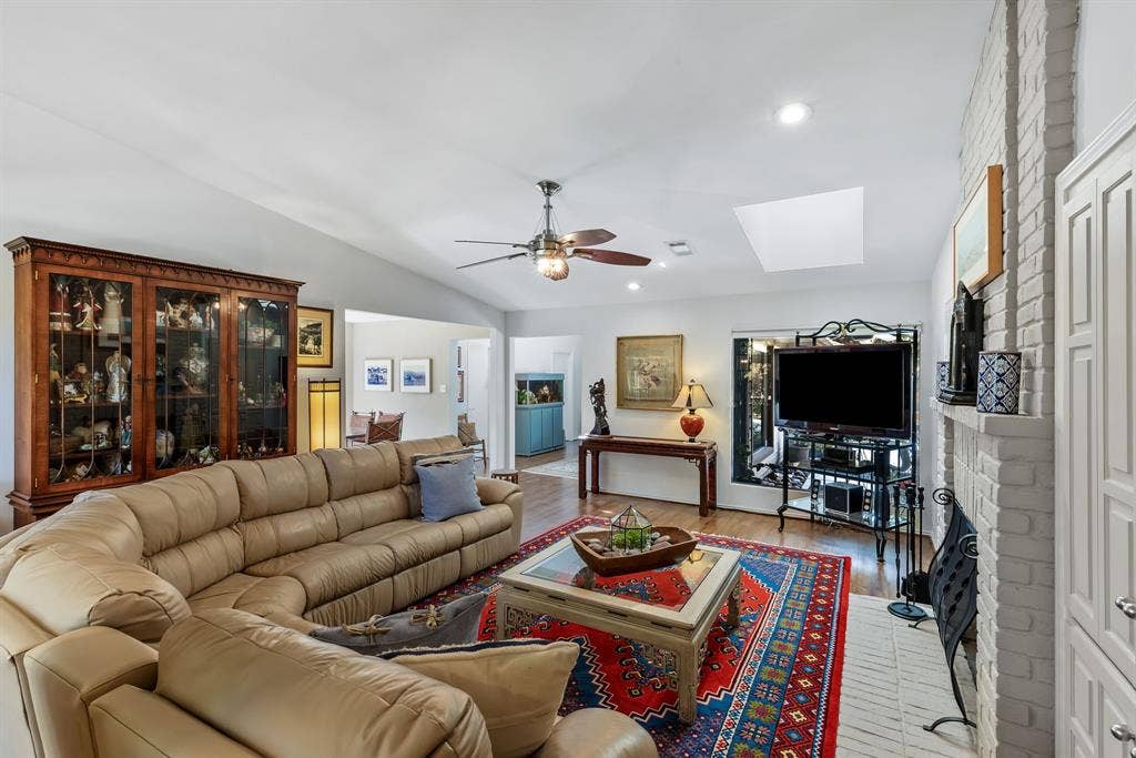 6803 Fernshaw Drive, Dallas, TX 75248 Vaulted ceiling with a ceiling fan, recessed lighting, wood-finish flooring, white brick fireplace with mantel, and a skylight