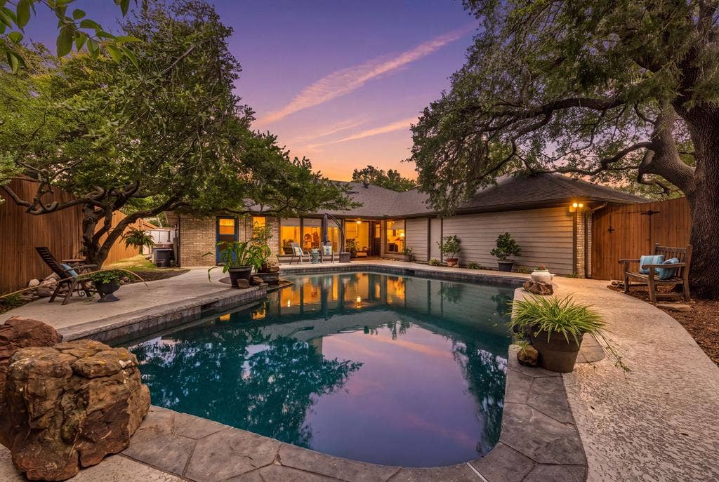 6803 Fernshaw Drive, Dallas, TX 75248 Swimming pool with stamped concrete decking, surrounded by mature trees and a private wooden fence