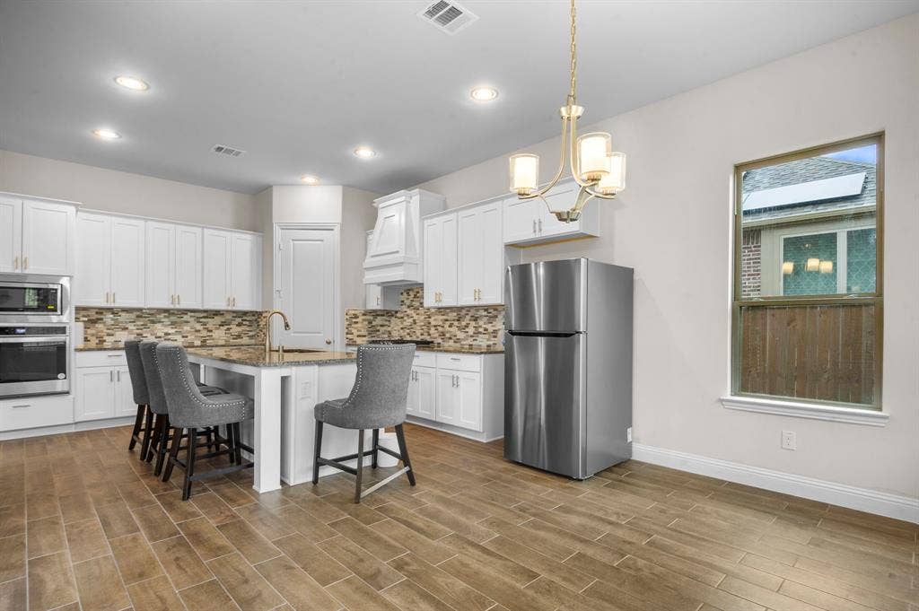 16050 Talamore Lane, Frisco, TX 75035 Kitchen with an island with sink, a breakfast bar, appliances with stainless steel finishes, and white cabinets