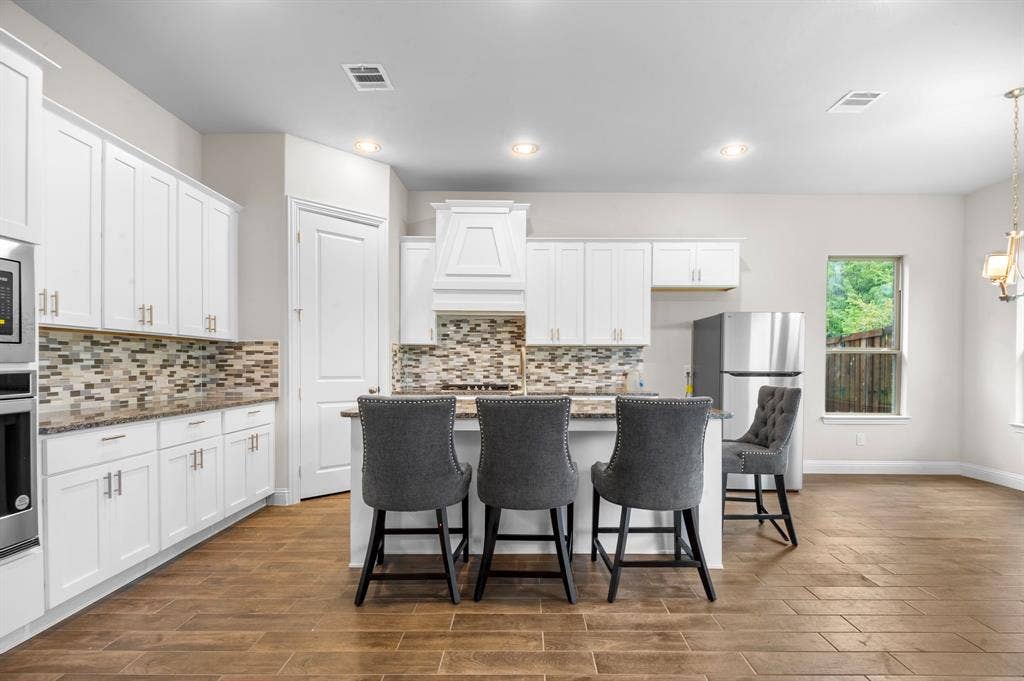 16050 Talamore Lane, Frisco, TX 75035 Kitchen with white cabinets, stainless steel appliances, dark hardwood / wood-style floors, dark stone counters, and a center island with sink
