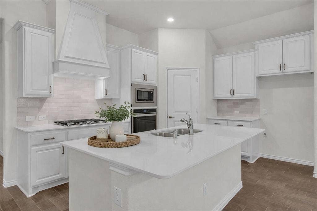 3106 Maverick Drive, Heath, TX 75126 Modern kitchen featuring a large central island with an undermount sink, white cabinetry, integrated stainless steel appliances, a tile backsplash, and wood-finish flooring