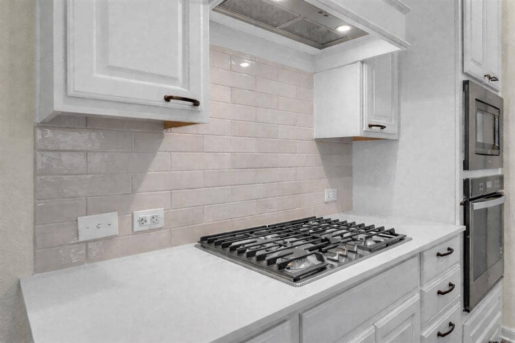3106 Maverick Drive, Heath, TX 75126 Kitchen with stainless steel gas cooktop, light-toned subway tile backsplash, white shaker cabinetry, and light-toned countertops