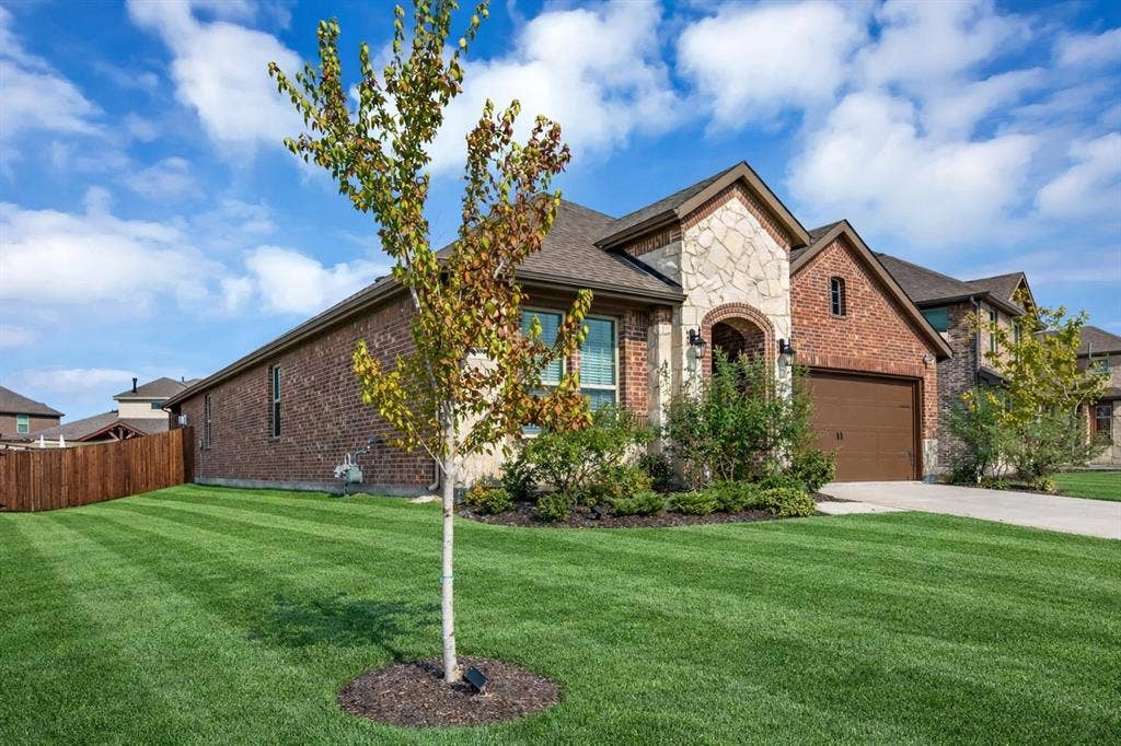 3106 Maverick Drive, Heath, TX 75126 Stone and brick facade featuring an arched entryway, attached two-car garage, concrete driveway, and manicured front lawn
