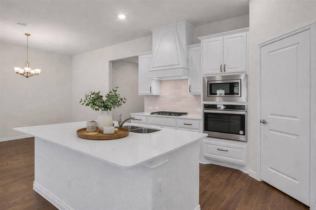 3106 Maverick Drive, Heath, TX 75126 White kitchen island with an undermount sink, a gas cooktop, white shaker cabinetry, stainless steel built-in appliances, and wood-finish flooring