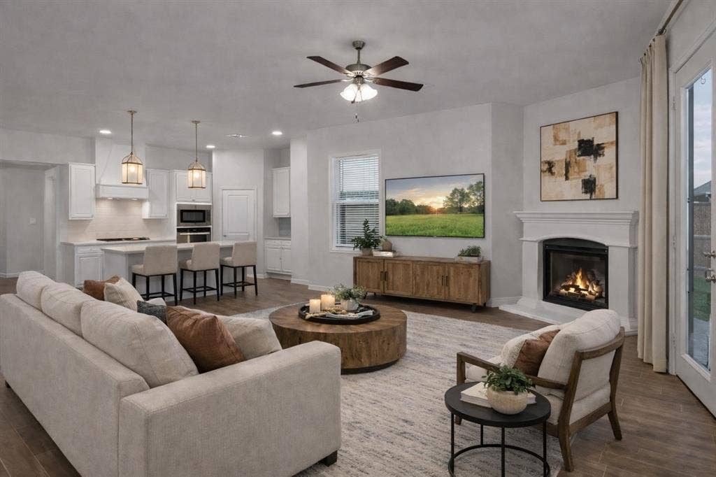 3106 Maverick Drive, Heath, TX 75126 Open-concept living space featuring a white kitchen with an island, a built-in fireplace, wood-finish flooring, and a ceiling fan