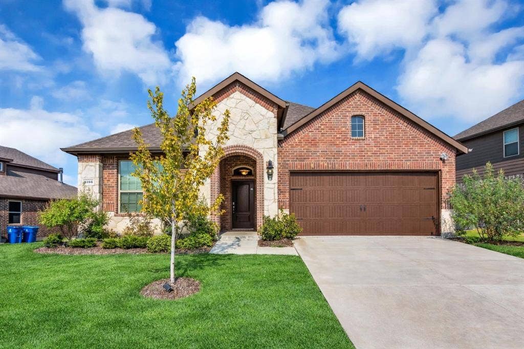 3106 Maverick Drive, Heath, TX 75126 Brick and stone facade featuring a prominent arched entryway, a two-car garage with a panel door, a concrete driveway, and a landscaped front yard with a young tree