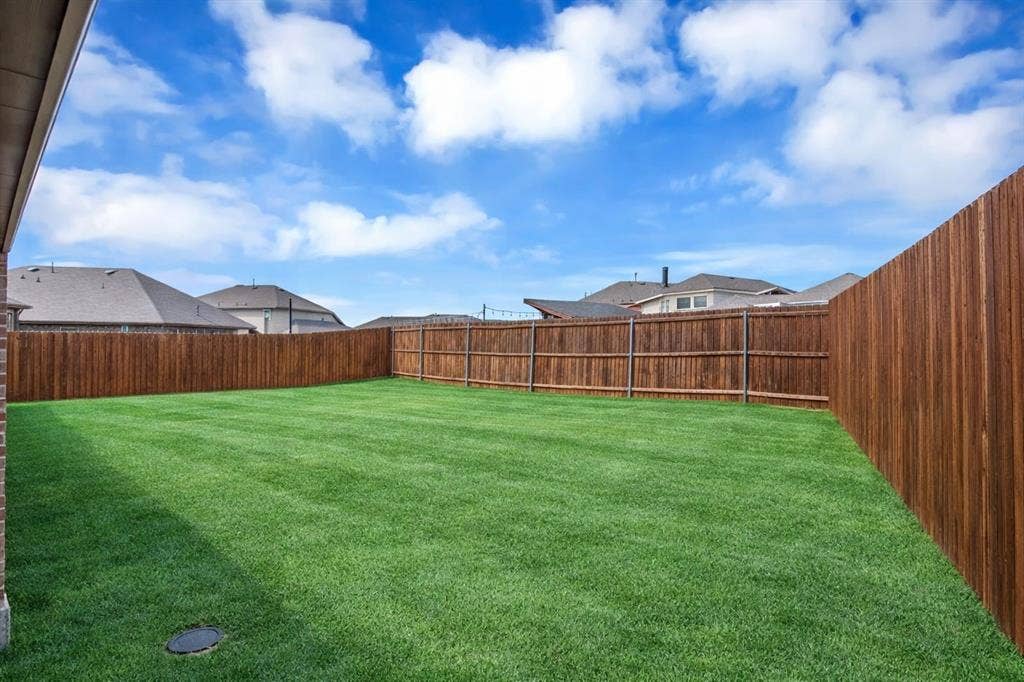 3106 Maverick Drive, Heath, TX 75126 Expansive backyard featuring a manicured lawn, a stained wood privacy fence, and brick detailing on the property exterior