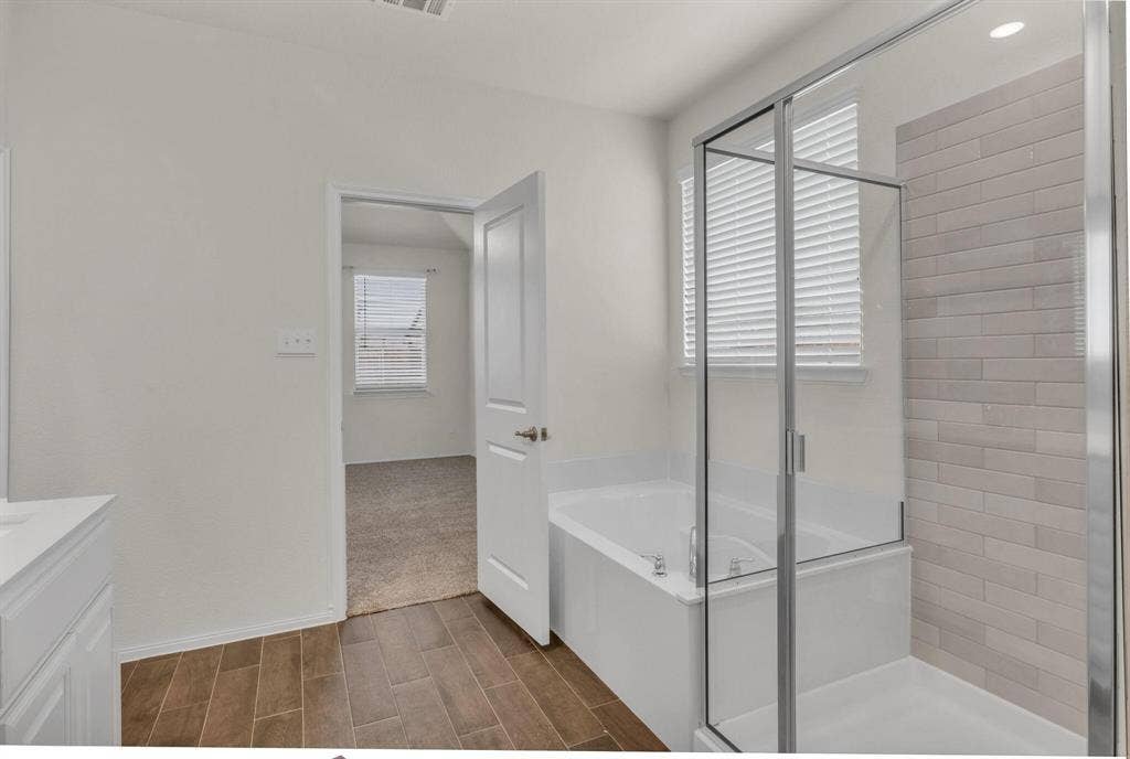 3106 Maverick Drive, Heath, TX 75126 Bathroom featuring a built-in tub, separate glass-enclosed shower with subway tile surround, wood-finish tile flooring, and light-toned vanity with countertop