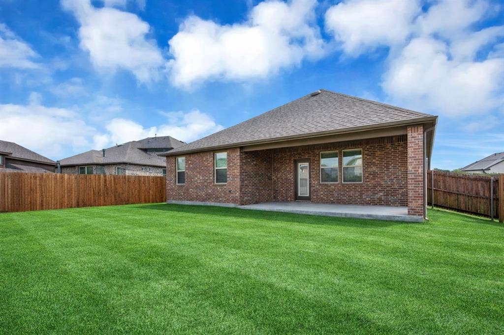 3106 Maverick Drive, Heath, TX 75126 Expansive green lawn with a covered concrete patio, full brick exterior, multiple windows, and a wood privacy fence