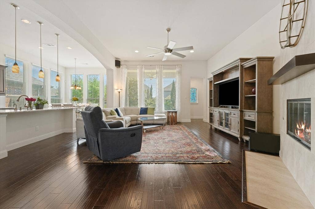 1113 5th Street, Argyle, TX 76226 Open living room with a gas fireplace, engineered hardwood flooring, tall windows and direct views into the kitchen and breakfast area.