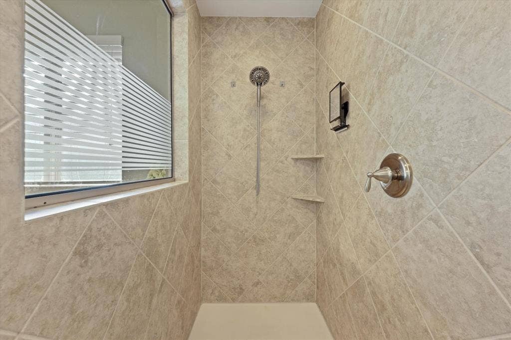 1113 5th Street, Argyle, TX 76226 Oversized tiled walk-in shower with built-in shelving, handheld showerhead and private window for natural light.