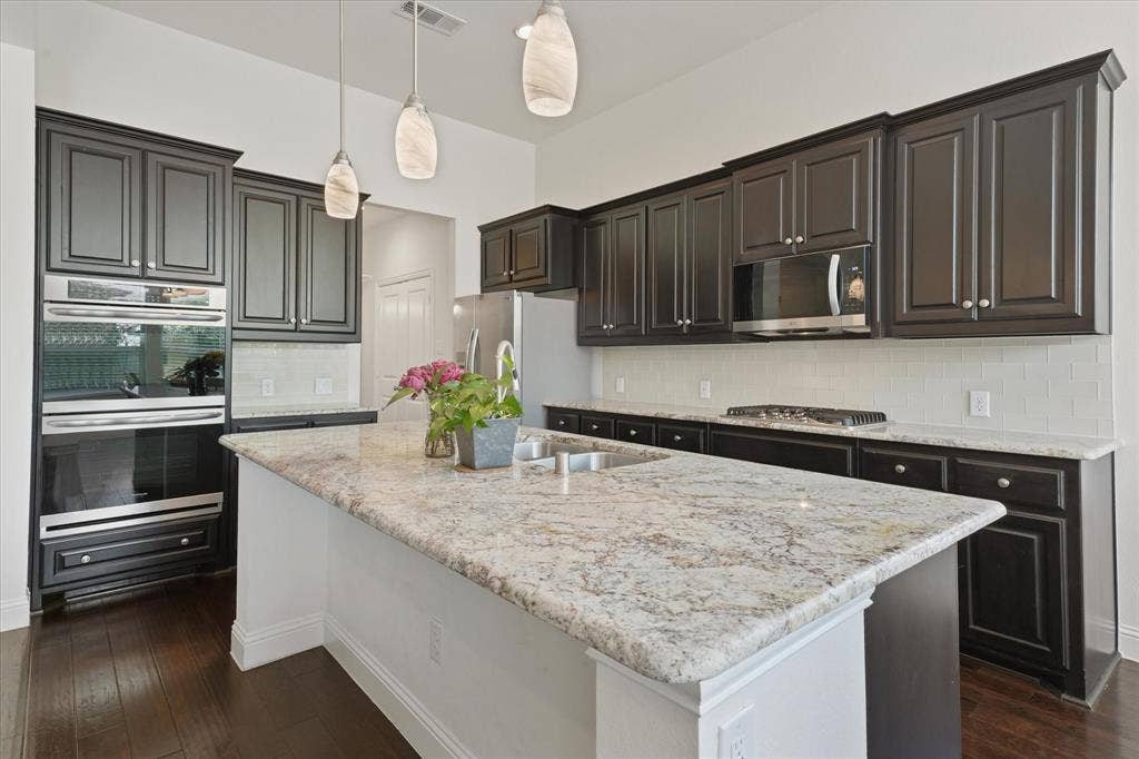 1113 5th Street, Argyle, TX 76226 Large granite kitchen island with sink, dishwasher, seating space and open sightlines to the main living area.