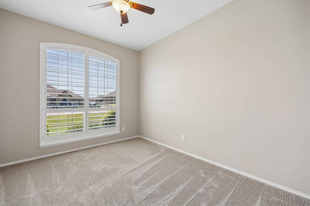 A spacious front bedroom filled with natural light, featuring plantation shutters, tall ceilings, and plush carpeting—perfect for guests, a nursery, or growing children.