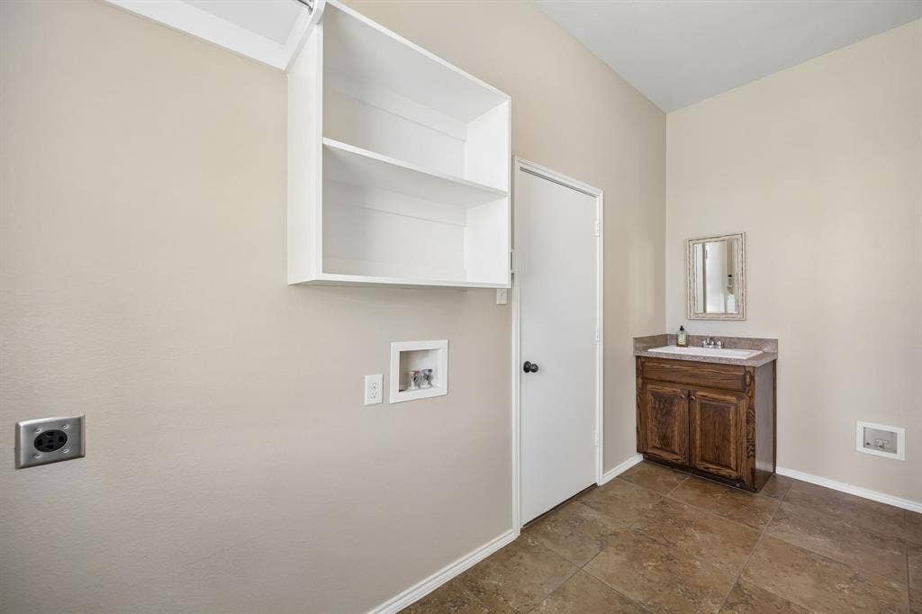 Spacious laundry room featuring built-in upper storage, utility sink with cabinet, washer/dryer connections, and plenty of room for organization and additional storage. This room also features a water line so you may have a refrigerator with a water dispenser and ice maker.