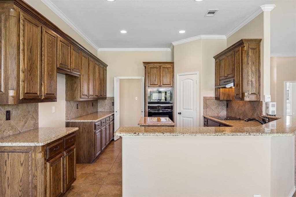 Chef-inspired kitchen with rich custom wood cabinetry, granite countertops, oversized island, abundant prep space, built-in appliances, walk-in pantry, and an open layout ideal for entertaining.