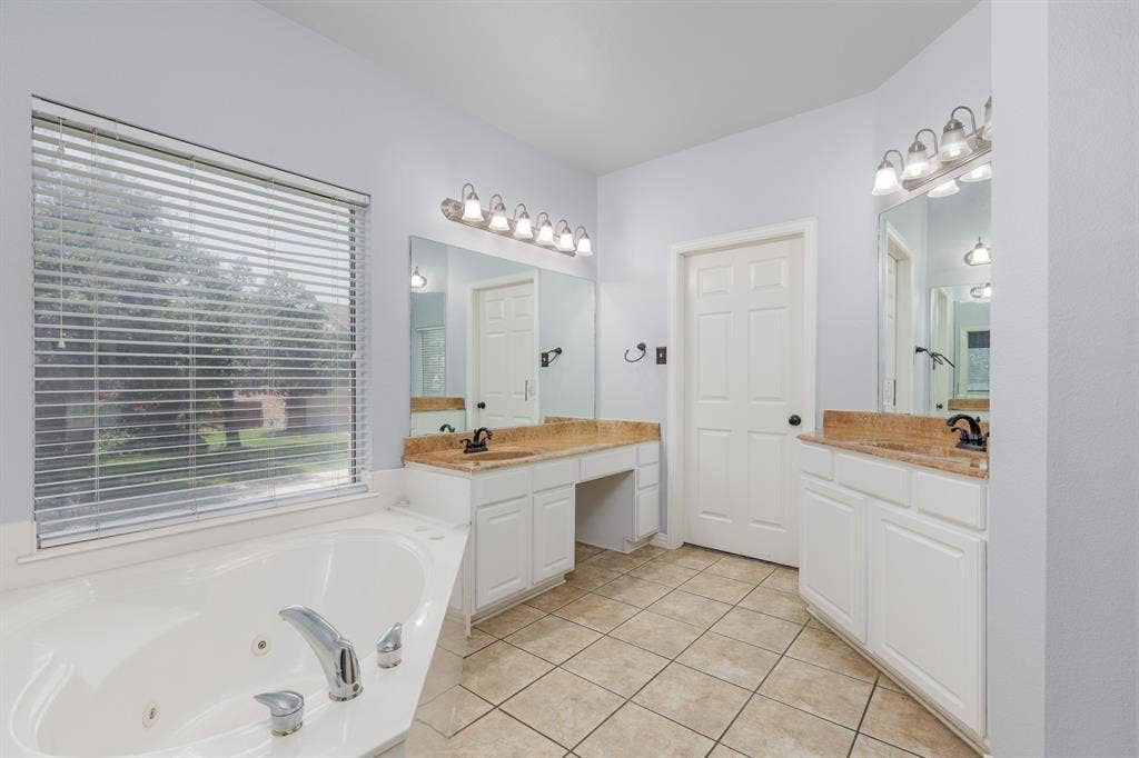 1913 Abilene Way, McKinney, TX 75072 Bathroom featuring a built-in jetted tub, dual vanity areas with integrated sinks and stone-finish countertops, tile flooring, and a large window with blinds