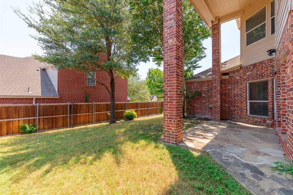 1913 Abilene Way, McKinney, TX 75072 Expansive backyard featuring a wood fence, mature tree, and a covered patio with flagstone flooring