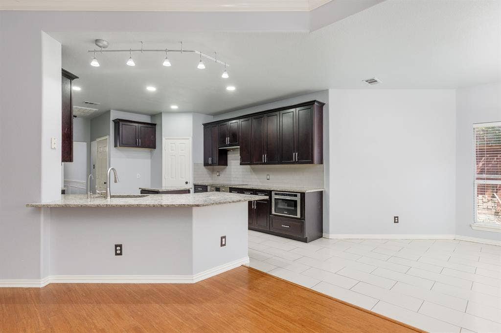 1913 Abilene Way, McKinney, TX 75072 Kitchen featuring dark wood cabinetry, light-toned countertops, a stainless steel under-mount sink with a high-arc faucet, a built-in microwave, and track lighting