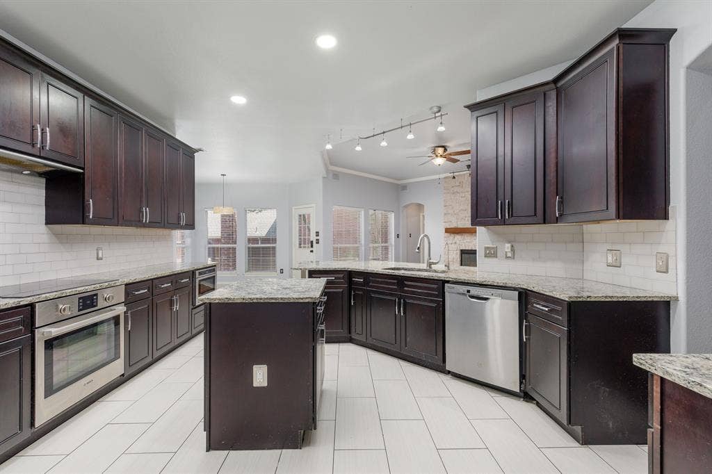 1913 Abilene Way, McKinney, TX 75072 Spacious chef's kitchen featuring dark wood cabinetry with brushed nickel hardware, stainless steel appliances, and a large center island with stone countertops