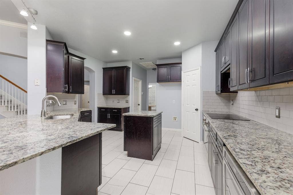 1913 Abilene Way, McKinney, TX 75072 Chef's kitchen featuring dual islands with granite countertops, dark cabinetry with contrasting white upper cabinets, stainless steel appliances, subway tile backsplash, recessed lighting, and tile flooring throughout the open layout