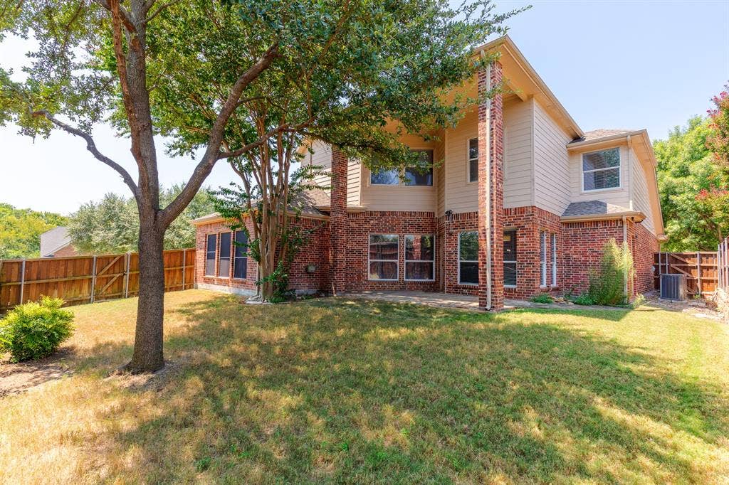 1913 Abilene Way, McKinney, TX 75072 Rear exterior featuring brick and siding construction, a substantial mature tree, a privacy fence, and multiple windows across two levels