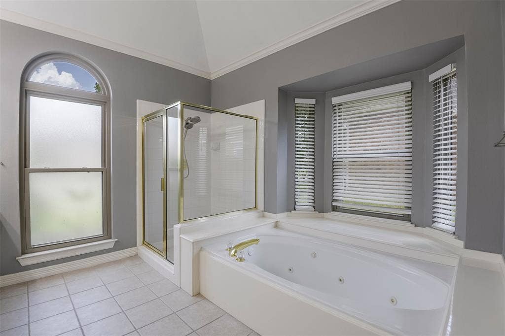 1200 Lakeway Drive, Plano, TX 75075 Soaking tub with integrated jets, glass-enclosed shower with brass accents, arched window, bay window, and tile flooring