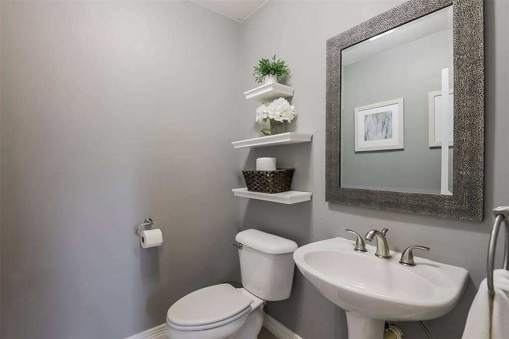 1200 Lakeway Drive, Plano, TX 75075 Pedestal sink with a brushed nickel faucet, framed mirror, and floating wall shelves