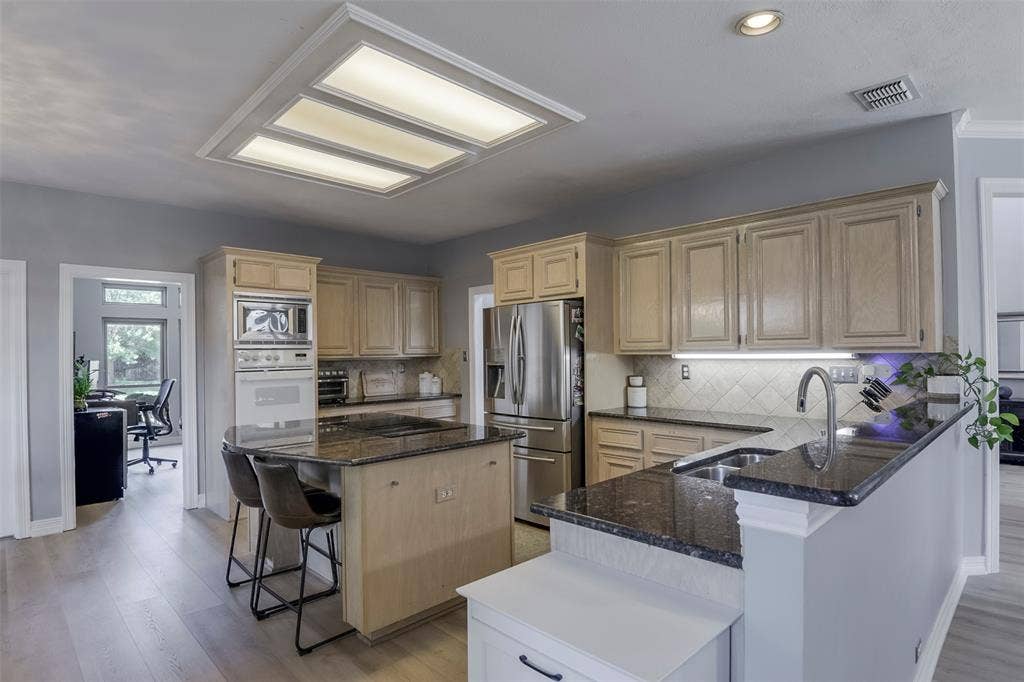 1200 Lakeway Drive, Plano, TX 75075 Kitchen with light wood-finish cabinetry, dark stone countertops, tile backsplash, stainless steel appliances, and a central island