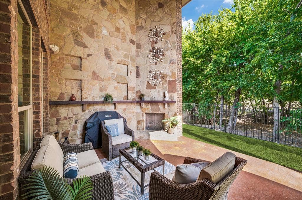 Enjoy this exquisite outdoor living space, which features a two-story covered patio, a stone-clad wall, and an integrated fireplace with scenic views of the trees.