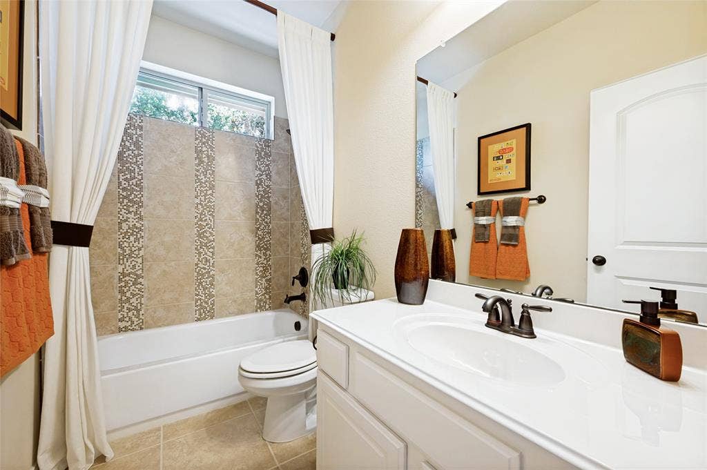 An upstairs bathroom features a bathtub with a tiled surround and decorative vertical accents, a vanity with an integrated sink, a bronze-finish faucet, and a full-width mirror.