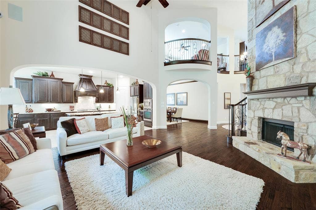 Expansive open-concept design featuring wood-finish flooring, a stone-clad fireplace with mantel, and an arched entryway to the kitchen