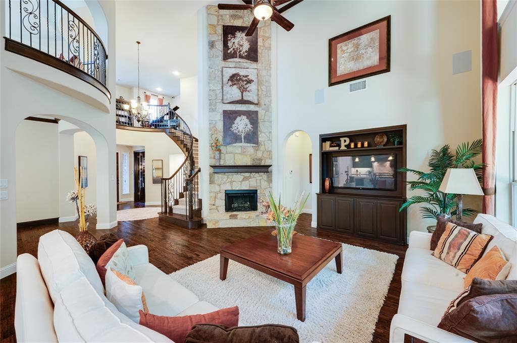 This expansive two-story living area features a stone-clad gas fireplace with gas logs, hand scraped hardwood flooring, and a custom built-in media center.