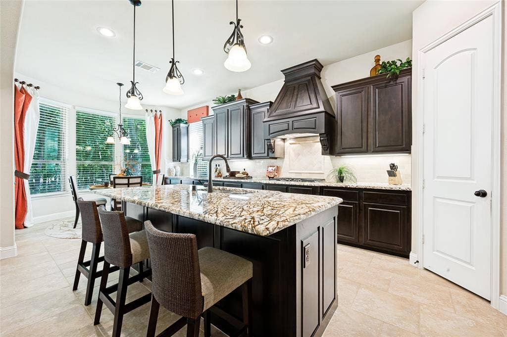 The gourmet kitchen features an open concept layout seamlessly flowing into the family room, complete with a central island, granite countertops, an integrated sink, custom wood cabinetry, a decorative range hood, recessed and pendant lighting, and a spacious walk-in pantry.