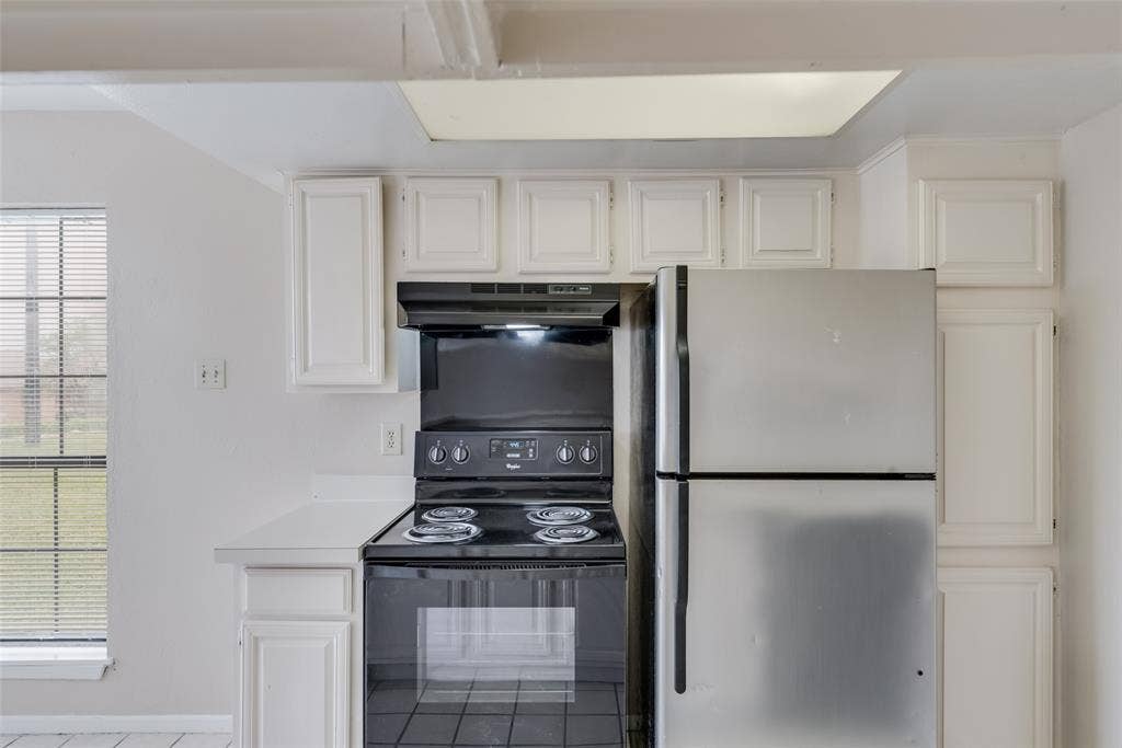 Kitchen featuring white cabinets, black range with electric cooktop, stainless steel fridge, and plenty of natural light