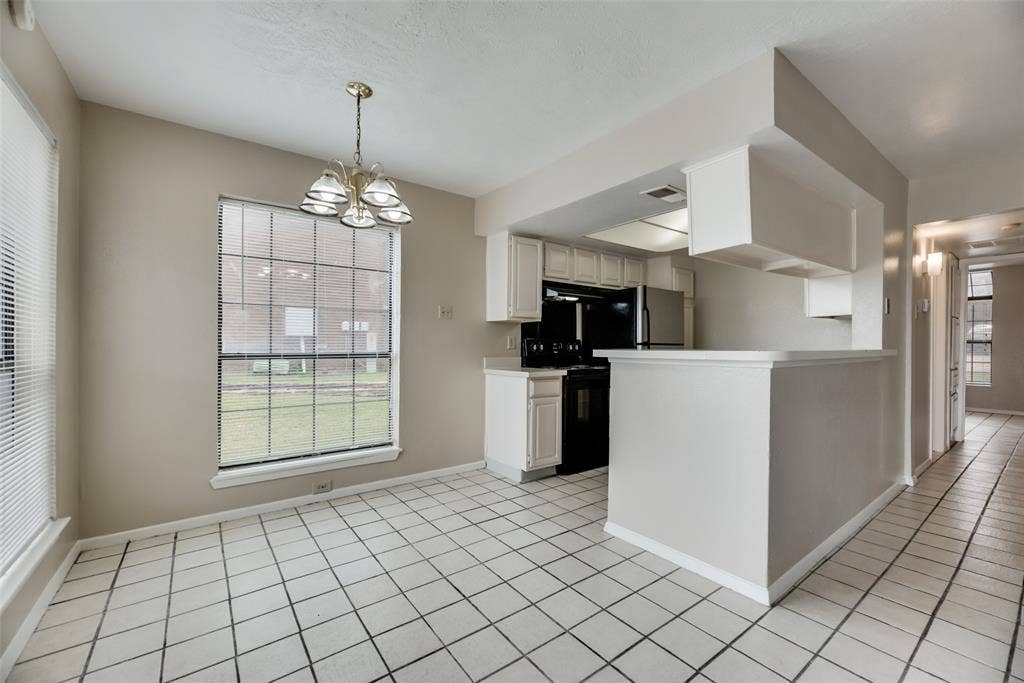Kitchen with pendant lighting, white cabinets, light tile flooring, black range with electric cooktop, and a notable chandelier