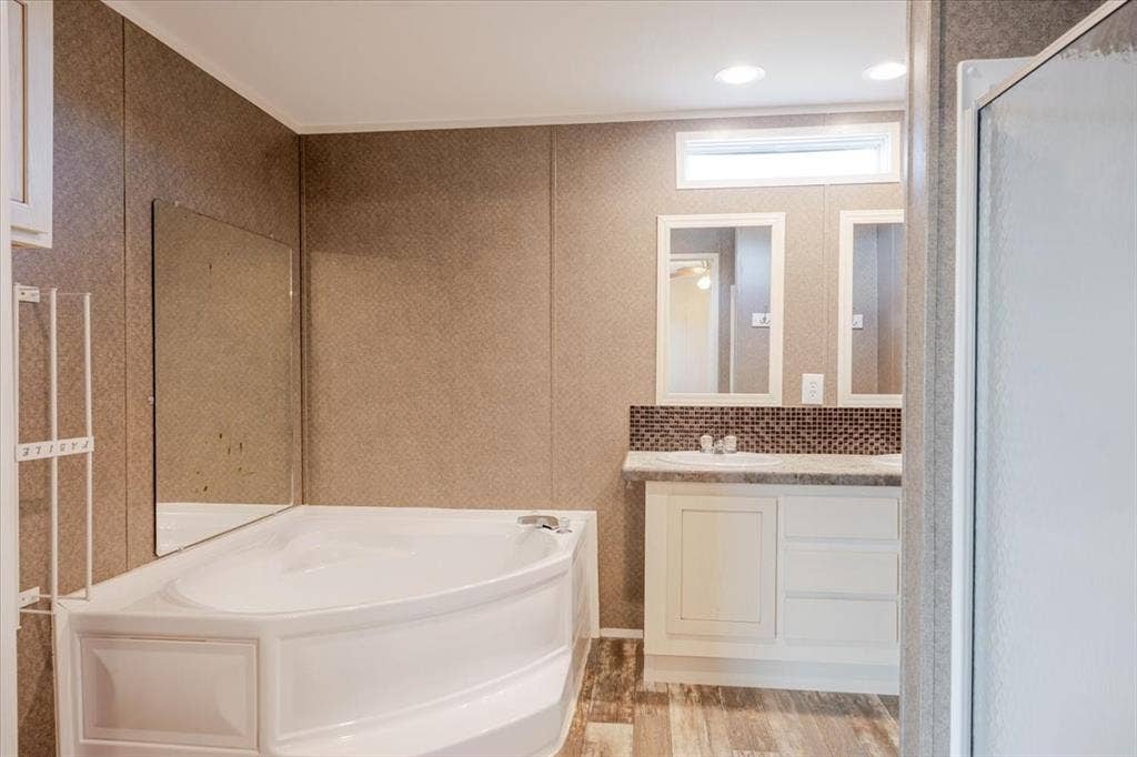 126 Starry Sky Court, Springtown, TX 76082 Corner garden tub alongside a dual-sink vanity with white cabinetry, mosaic tile backsplash, and individual framed mirrors.