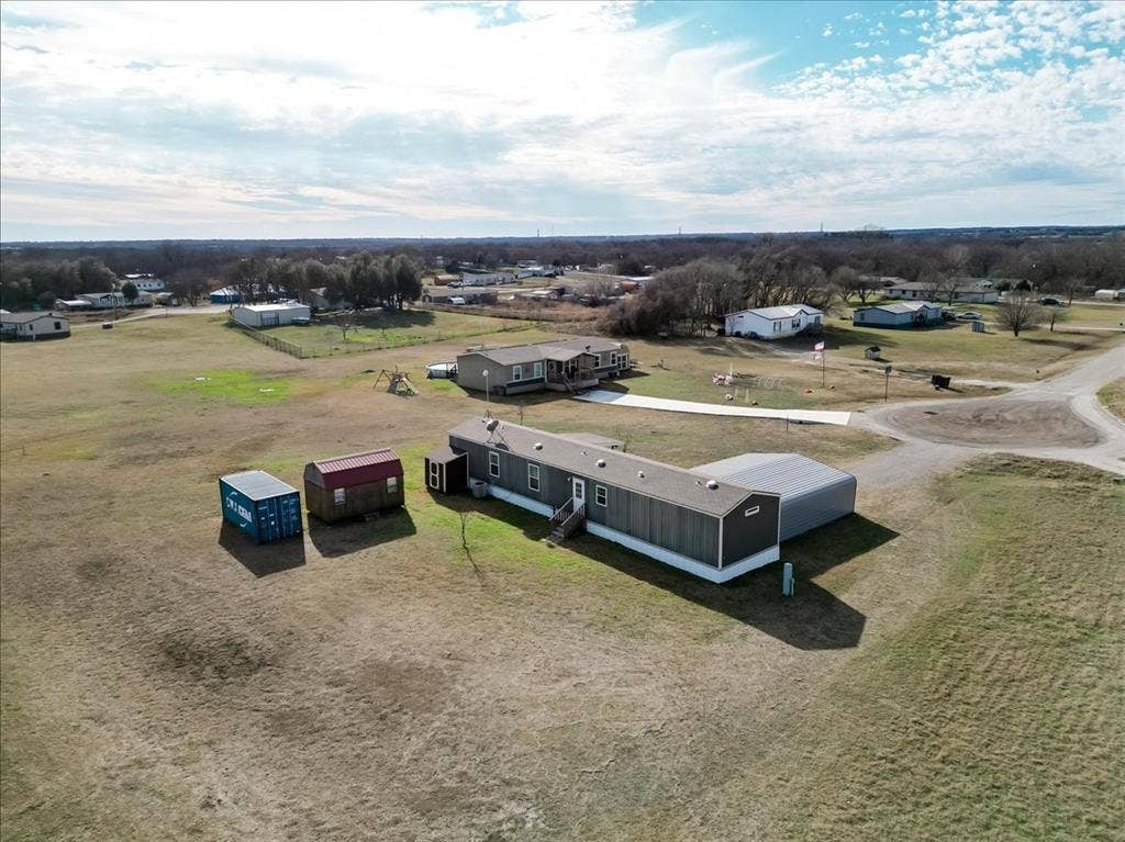 126 Starry Sky Court, Springtown, TX 76082 Expansive property featuring grey mobile home with a white skirting, a covered carport, Convex storage unit and wooden work show with electricity. Water filtering system is on the back of the mobile home.