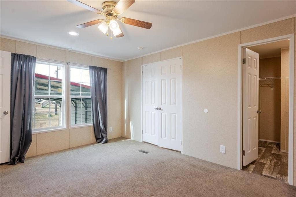 126 Starry Sky Court, Springtown, TX 76082 Carpeted interior room featuring a ceiling fan with light fixture, two windows with curtains, a built-in closet with bifold doors, and an additional open closet with wood-finish flooring
