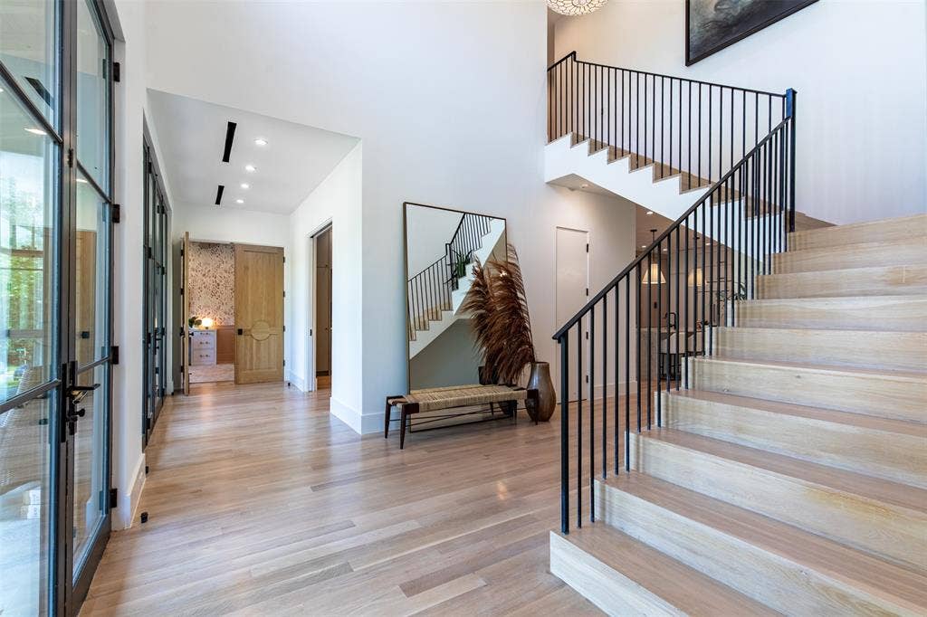 6979 Bob O Link Drive, Dallas, TX 75214 Light wood-finish flooring extending through a spacious entryway featuring an open staircase with black iron railings, a wall of glass-paned doors, recessed lighting, and a chandelier