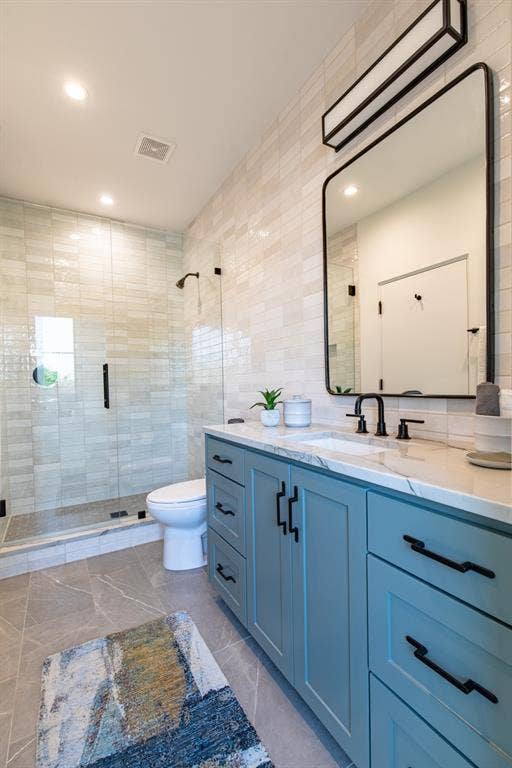 6979 Bob O Link Drive, Dallas, TX 75214 Bathroom featuring a light blue vanity with black hardware, a rectangular mirror, and a glass-enclosed shower with black fixtures