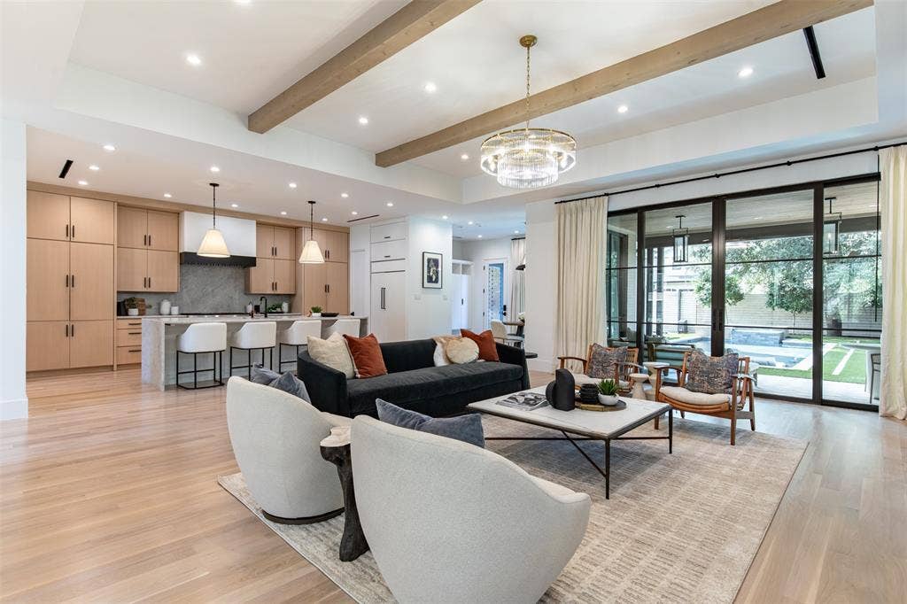 6979 Bob O Link Drive, Dallas, TX 75214 Spacious living area featuring light wood-finish flooring, exposed ceiling beams, and a contemporary chandelier