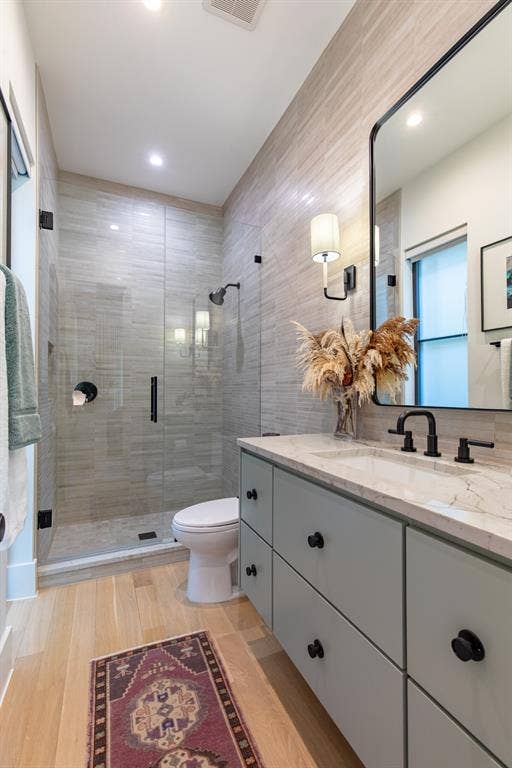 6979 Bob O Link Drive, Dallas, TX 75214 Modern bathroom featuring a glass-enclosed shower with tile surround, light wood-finish flooring, a double vanity with light gray cabinetry, a white countertop, and a large wall-mounted mirror
