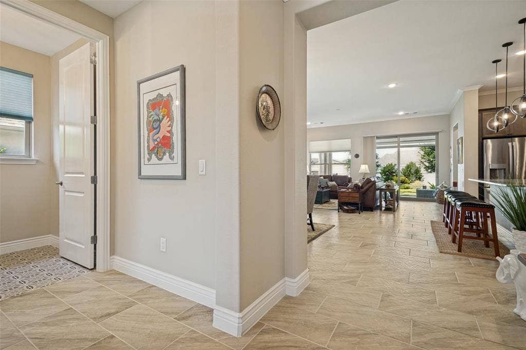 FROM THE ENTRY A GLANCE INTO THE LIVING AREA AND A HALF BATH IS ADJACENT AND FINISHED WITH FRAMED MIRROR, DESIGNER LIGHTING AND CERAMIC TILE IN A WHIMSICAL NEUTRAL PATTERN.