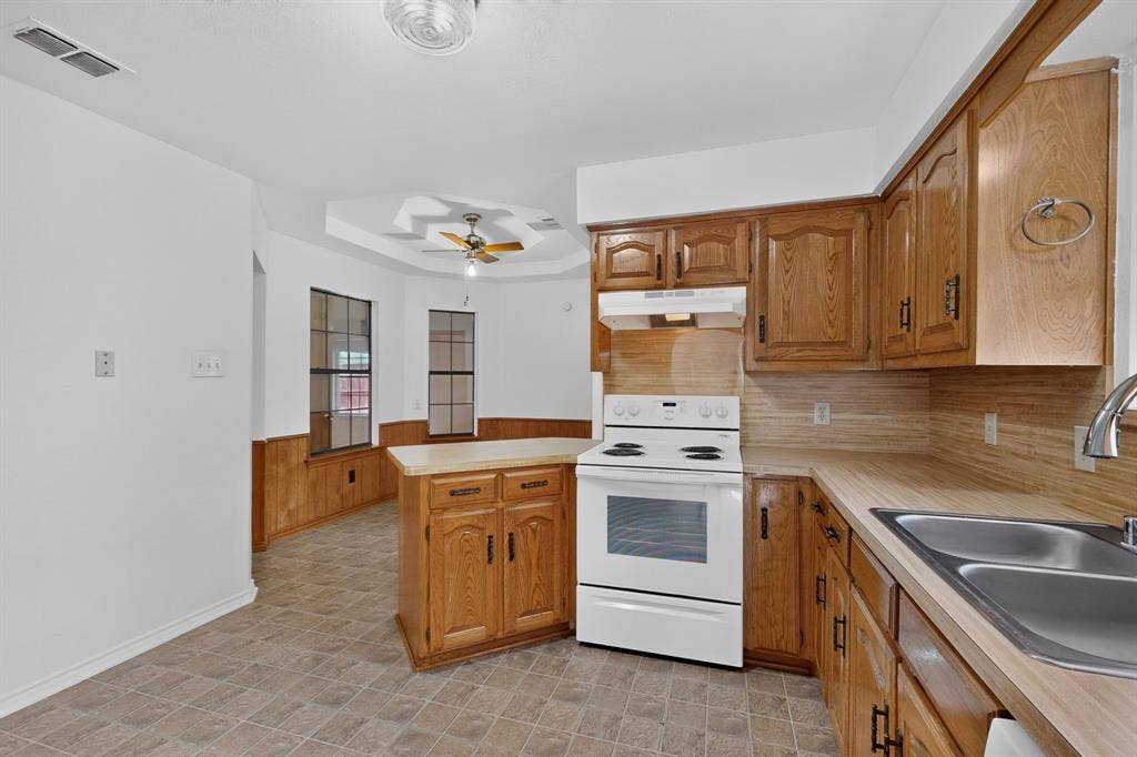 303 Stoneybrook Drive, Wylie, TX 75098 Kitchen featuring wood cabinetry, white electric range, double basin stainless steel sink, and light-toned countertops
